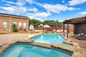 Un patio trasero con piscina, terraza de madera y edificio de ladrillo.