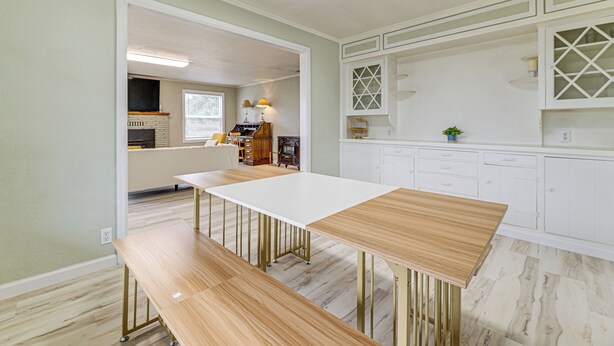 Une cuisine spacieuse avec une longue table et des bancs blancs, des meubles de cuisine blancs et un grand luminaire au plafond.