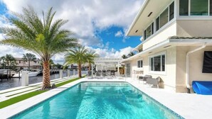 Ein moderner Poolbereich mit klarem Pool, Palmen und einem Gebäude mit Außenbestuhlung.