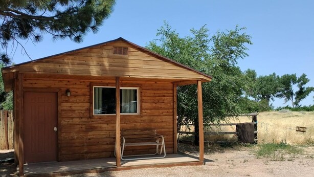 A wooden cabin with a single garage door, a bench outside, and a clear blue sky in the background.