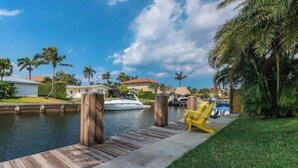 A waterfront property with a dock, a yellow chair, and a boat in the background. - Delray Beach Tropical Retreat (Delray Beach)
