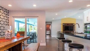 A modern kitchen with a central island, bar stools, and a dining area with a wooden table and chairs. - Delray Beach Tropical Retreat (Delray Beach)