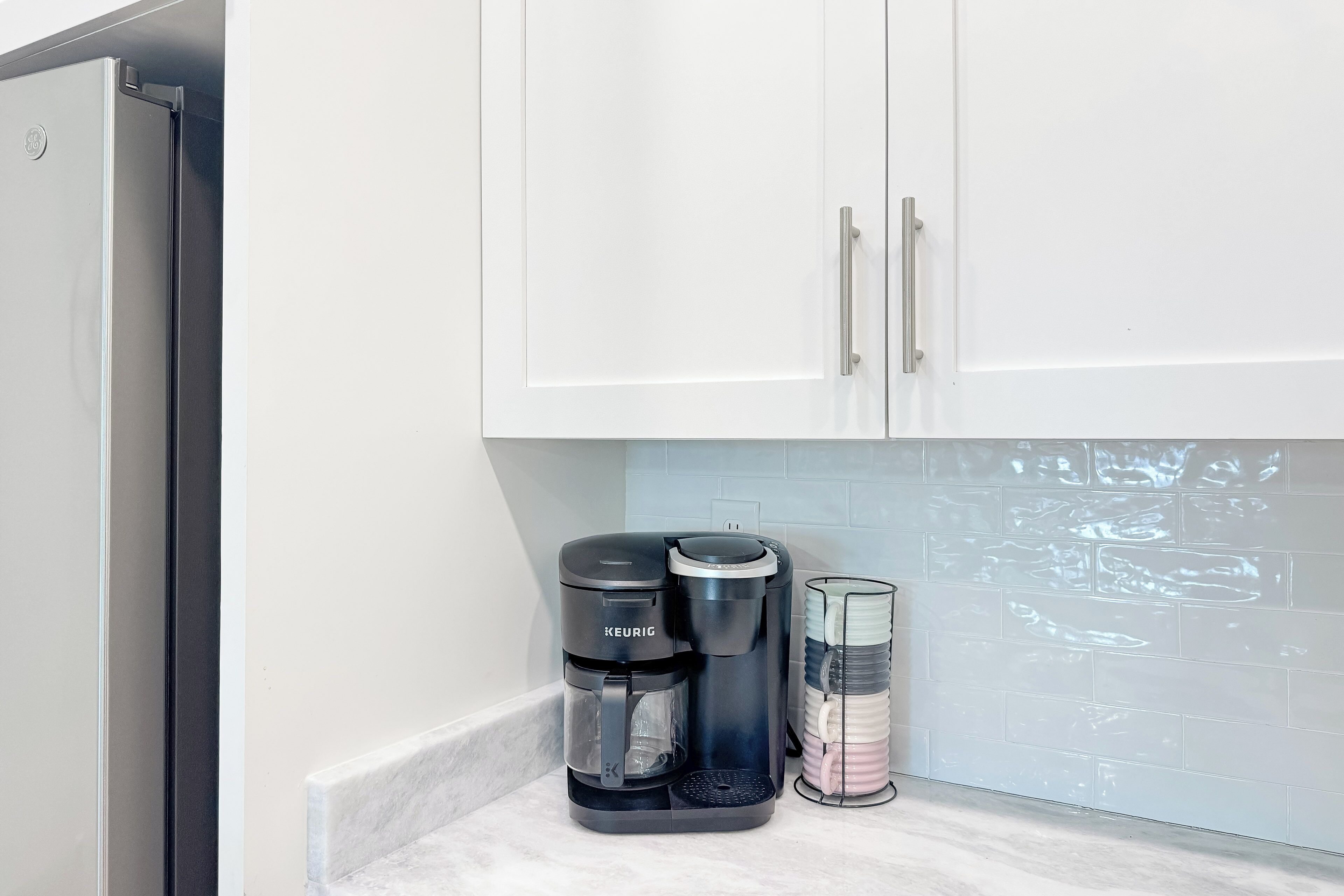 A kitchen with white cabinets, a black Keurig coffee maker, and a stainless steel coffee pot.