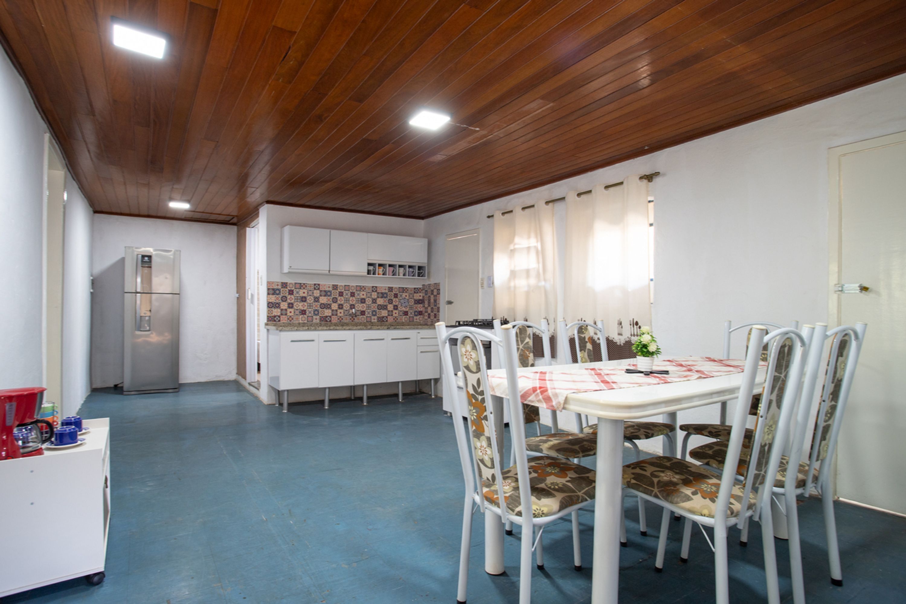 A dining area with a table and chairs, a refrigerator, and a kitchen in the background.