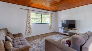 Una sala de estar con techo de madera, un ventanal con cortinas, un televisor de pantalla plana y dos sofás.