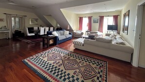 Ein geräumiges Wohnzimmer mit hoher Decke, einem Essbereich und einem großen Fenster mit Vorhängen.