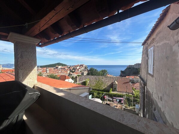 A balcony with a view of a coastal town, including a hill with buildings and a sea in the background.