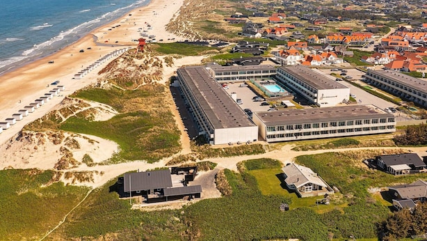 Luchtbeeld van een kustresort met toegang tot het strand, moderne gebouwen en een zwembad.