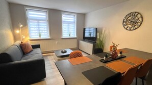 Una sala de estar moderna con un sofá, una mesa de comedor con sillas, un televisor y un reloj en la pared.