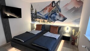 Un dormitorio moderno con una cama grande, un televisor montado y un mural con motivos de montaña en la pared.