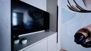 Una sala de estar moderna con un televisor de pantalla plana montado en un mueble blanco, una pequeña planta en maceta en la estantería y un gran mural en la pared con la imagen de un alce.
