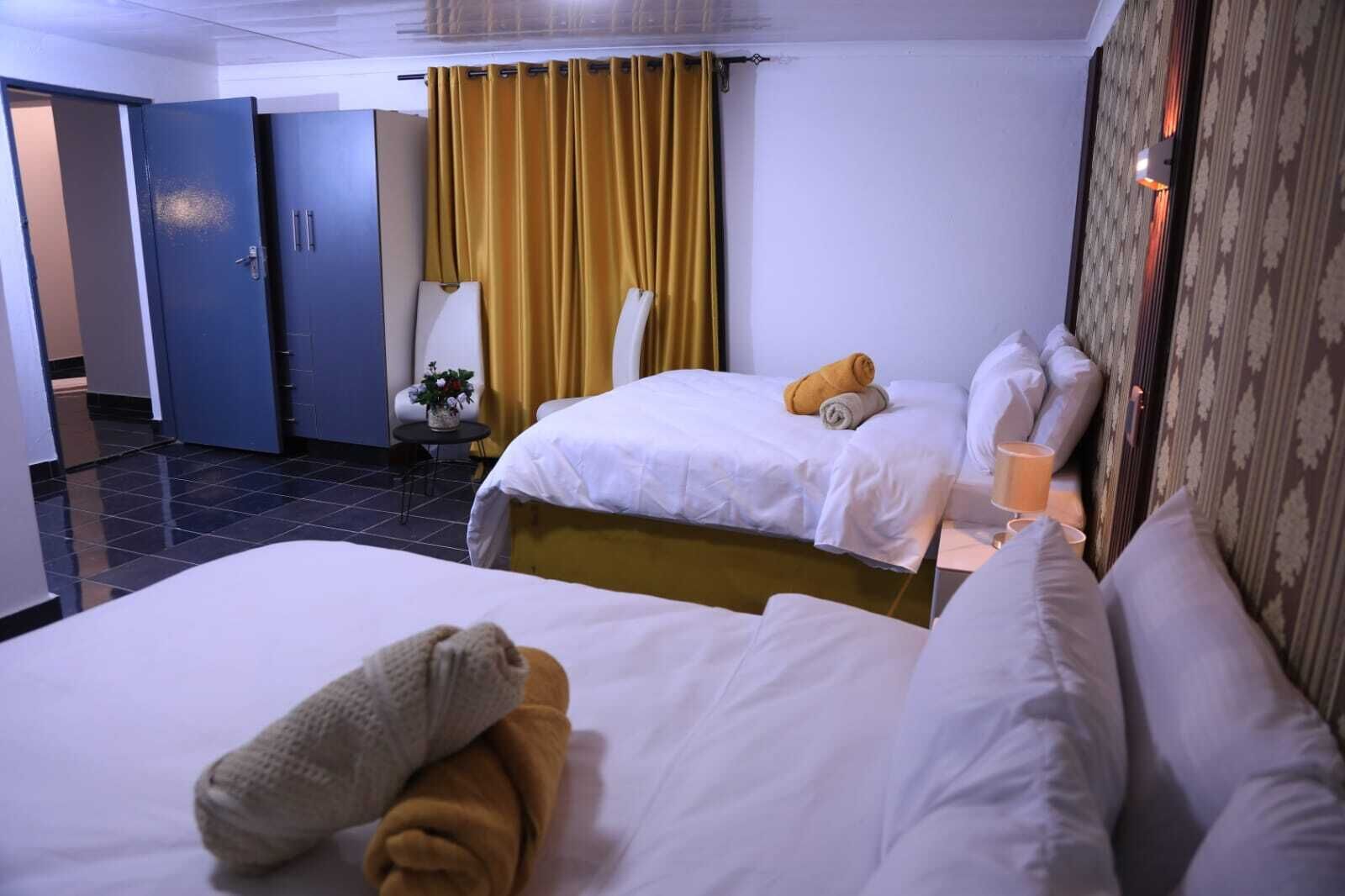 A hotel room with two beds, a chair, a small table with a plant, and a curtain.