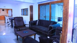 A living room with a sofa, armchairs, and a coffee table. There is a dining area with a table and chairs. - 12-bedroom bed guest house in charming Bedfordvew with WiFi, AC (Germiston)