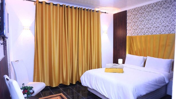 A hotel room with a bed, a chair, a small table with a plant, and a curtain. - 12-bedroom bed guest house in charming Bedfordvew with WiFi, AC (Germiston)