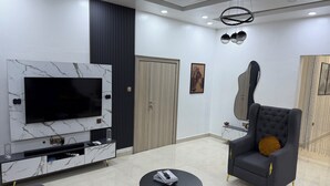 Una sala de estar moderna con televisor, mueble de entretenimiento, sofá, sillón y una mesita de centro.