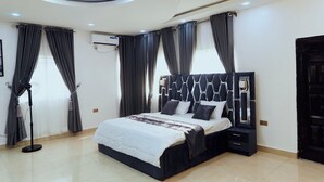 Een moderne slaapkamer met een groot bed, een donker hoofdbord en een staan ventilator.