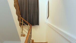 Una escalera de madera con barandilla, que conduce a un rellano con una cortina oscura.