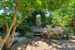 Un sendero en un jardín conduce a una escalera de piedra rodeada de abundante vegetación y plantas florecientes.