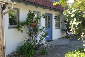 A white building with a blue door and windows, a stone pathway, and various plants. - Quiet 145sqm apartment with garden & 3 bedrooms - ideal for families & friends (Kißlegg)