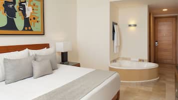Een hotelkamer met een groot bed, een nachtkastje met lamp, een schilderij aan de muur, en een aparte badkamer met bad.
