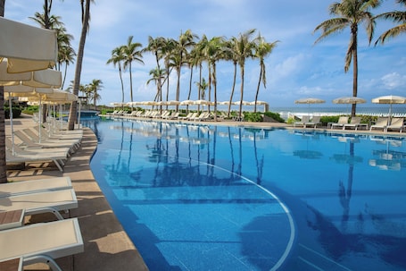 Una piscina al aire libre, sombrillas, sillones reclinables de piscina