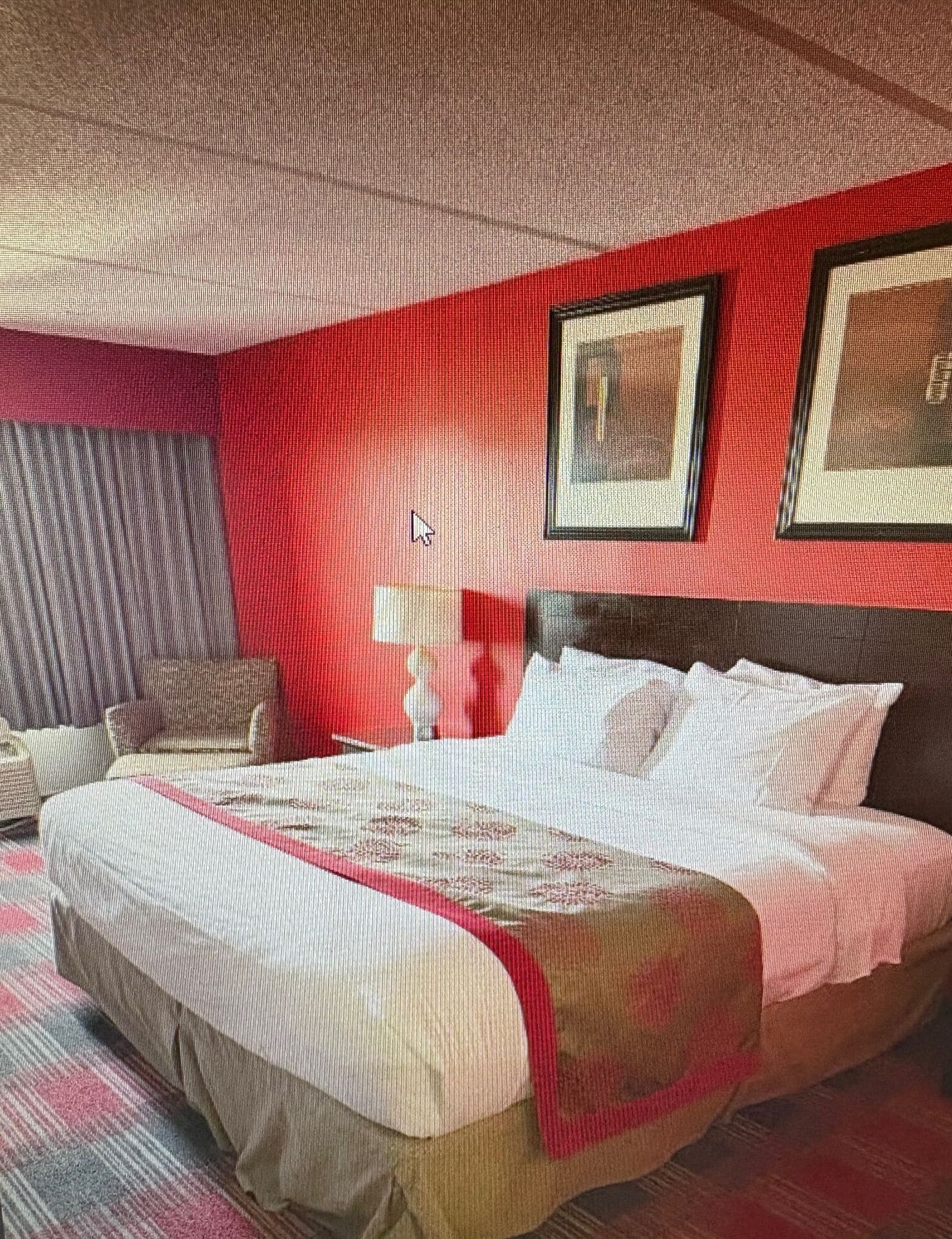 Quarto de hotel com uma cama, mesa de cabeceira, luminária e um quadro pendurado na parede.