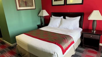 A hotel room with a large bed, two bedside tables, a red wall, and framed artwork on the wall.
