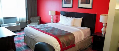A hotel room with a large bed, two bedside lamps, a chair, a desk, and a window with curtains.