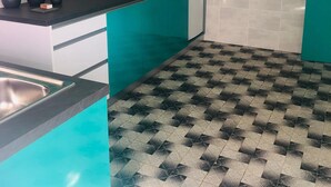 Een keuken met blauwgroene kastjes, een zwart aanrecht en een patroon vloer.