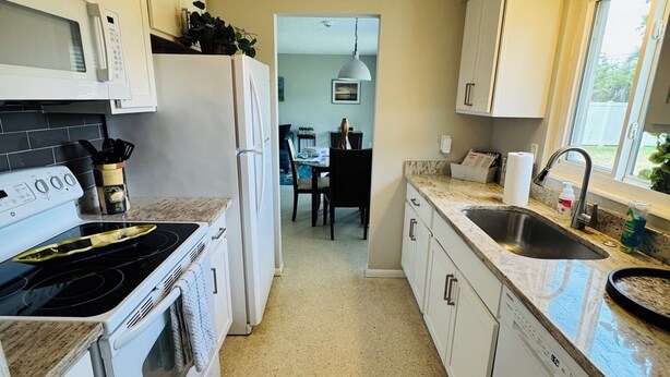 A kitchen with white cabinets, a stove, a microwave, a ceiling fan, and a window. - Entire place in the heart of Sarasota (Sarasota)