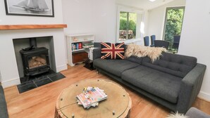 Ein Wohnzimmer mit Kamin, einer Couch, einem Couchtisch mit Zeitschriften, einem Bücherregal und einem gerahmten Bild an der Wand.