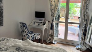 Ein Schlafzimmer mit Bett, Schreibtisch, Stuhl, Fernseher und Blick ins Freie durch eine Glastür.