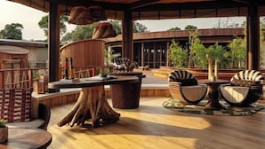 An outdoor seating area with round tables, wicker furniture, and a wooden deck. - The Ritz-Carlton, Masai Mara Safari Camp (MASAI MARA)