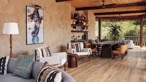 A spacious living area with a wooden floor, a sofa with patterned cushions, a coffee table, and a dining area with chairs and a table. - The Ritz-Carlton, Masai Mara Safari Camp (MASAI MARA)