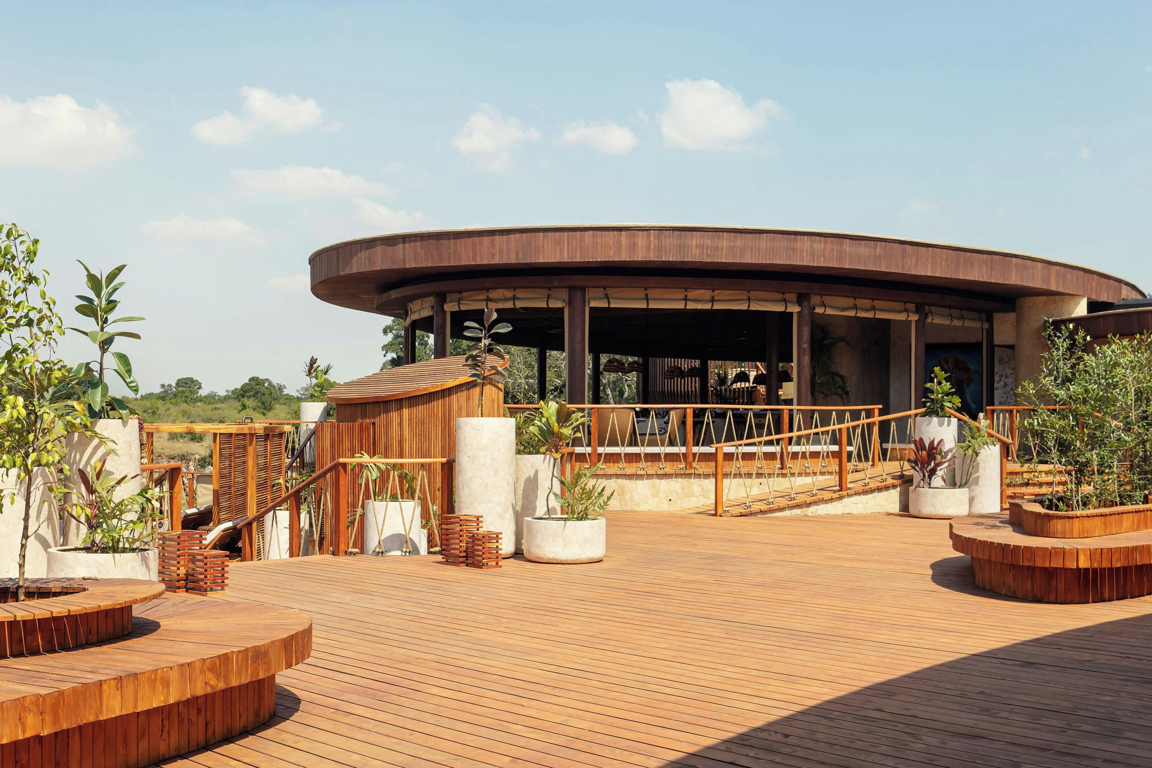 Eine Holzterrasse mit einem runden Gebäude, Sitzgelegenheiten im Freien und Blumentöpfen.