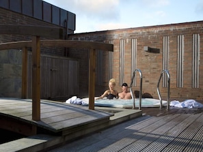A rooftop pool area with two people relaxing in the water, surrounded by wooden deck and a brick building. - 6 Person Holiday Home on a Holiday Park in Romo (Rømø)