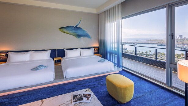 Habitación de hotel con dos camas, un ventanal con vista a la ciudad y un cuadro de una ballena en la pared.