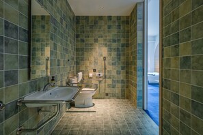 Een moderne badkamer met een groot wastafel, toilet en douchegedeelte, met groene betegelde wanden en vloer.
