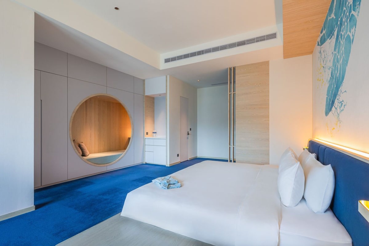 Una moderna camera d'albergo con un'area salotto circolare, un letto grande con lenzuola bianche e un tappeto blu.