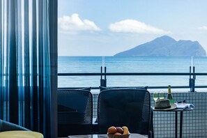 A dining area with a view of the sea and a mountain, featuring two chairs, a table with a bottle, glasses, and a bowl of fruit. - The Archipelago (Yilan County)