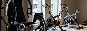 A gym with stationary bikes, exercise equipment, and a large window providing a view of the city.