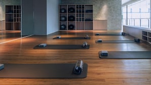 Una habitación amplia con suelo de madera, varias colchonetas de yoga y equipo de ejercicio.