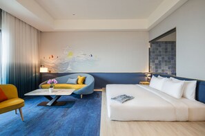 A modern hotel room with a blue sofa, a yellow armchair, a white bed, and a large abstract wall art piece. - The Archipelago (Yilan County)