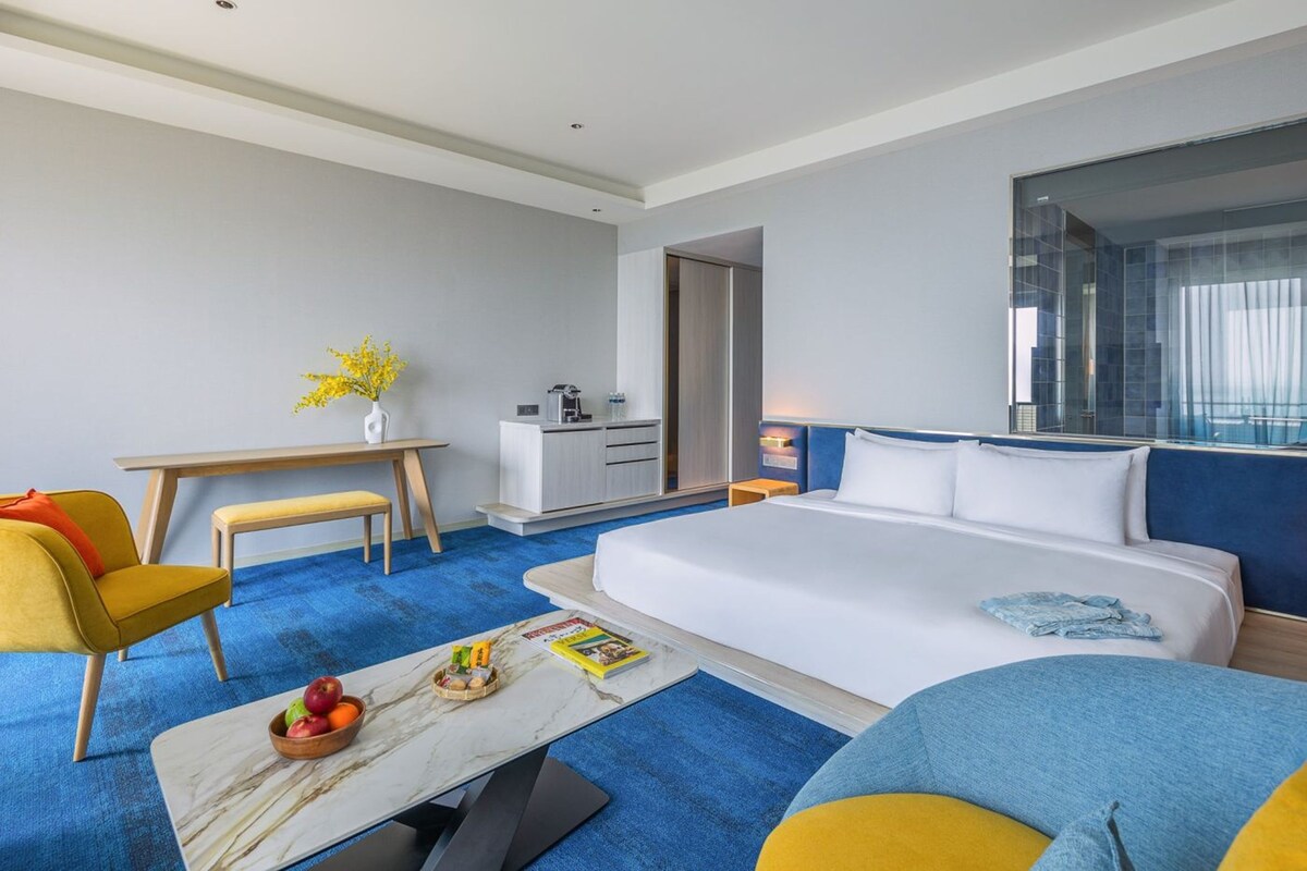 Una habitación de hotel con cama, escritorio, silla, cafetera y ventana.