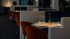 Un restaurante con una decoración moderna, que incluye sillas blancas y anaranjadas, mesas redondas y un suelo oscuro.