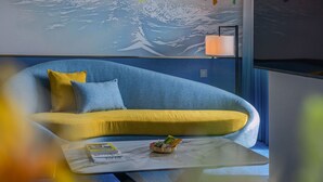 Una habitación moderna con un sofá azul, una mesita de centro pequeña y un mural en la pared que representa una playa.