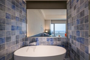Un baño moderno con una bañera grande, paredes con azulejos azules y vistas a un balcón a través de un espejo amplio.