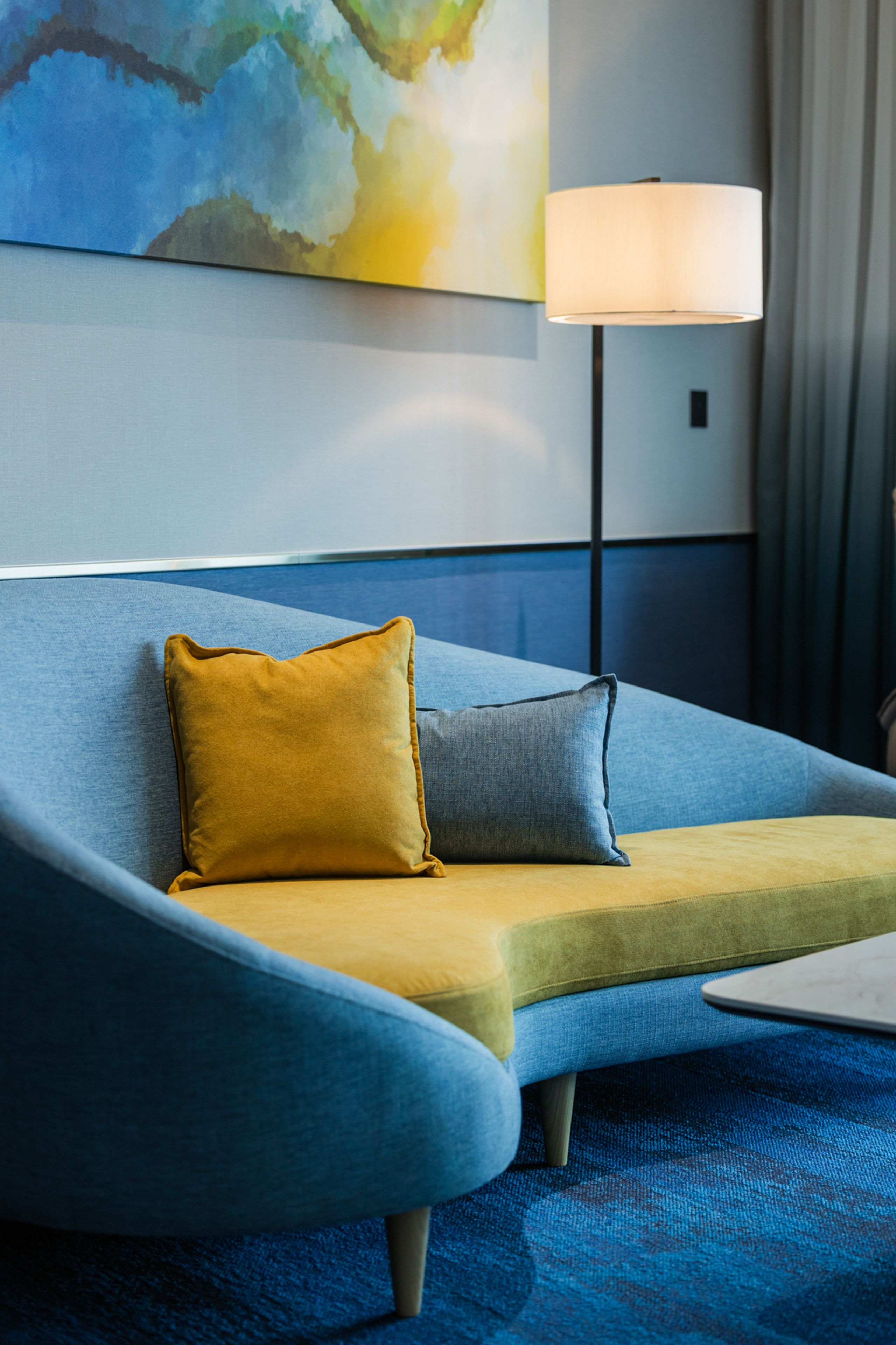 A modern hotel room with a blue sofa, a yellow pillow, and a grey pillow.