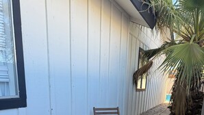 Une terrasse avec des meubles en bois et une petite table, un mur blanc et un palmier.