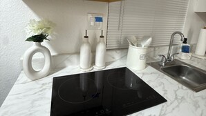 Une cuisine équipée d’une plaque de cuisson à induction intégrée, d’un évier et de meubles blancs.